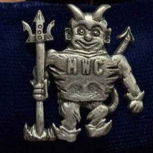 Sliver devil brooch with the letters MWC on its chest.