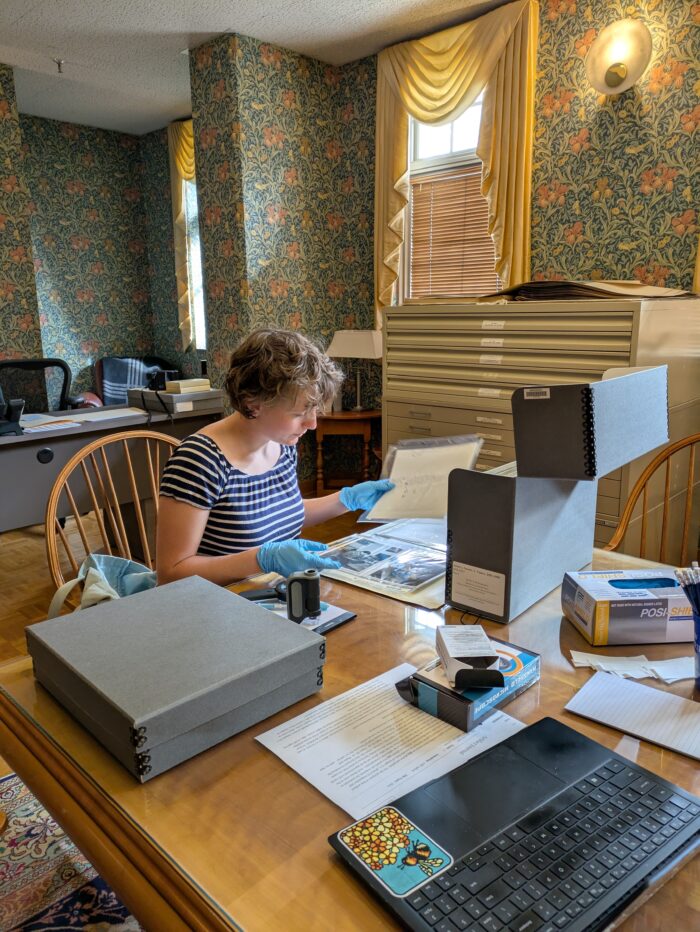 Person with short curly hair reviewing documents from an archival box at a desk in an office.