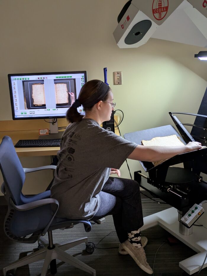 Student Sitting at a book scanner with computer in the background with scanning software open
