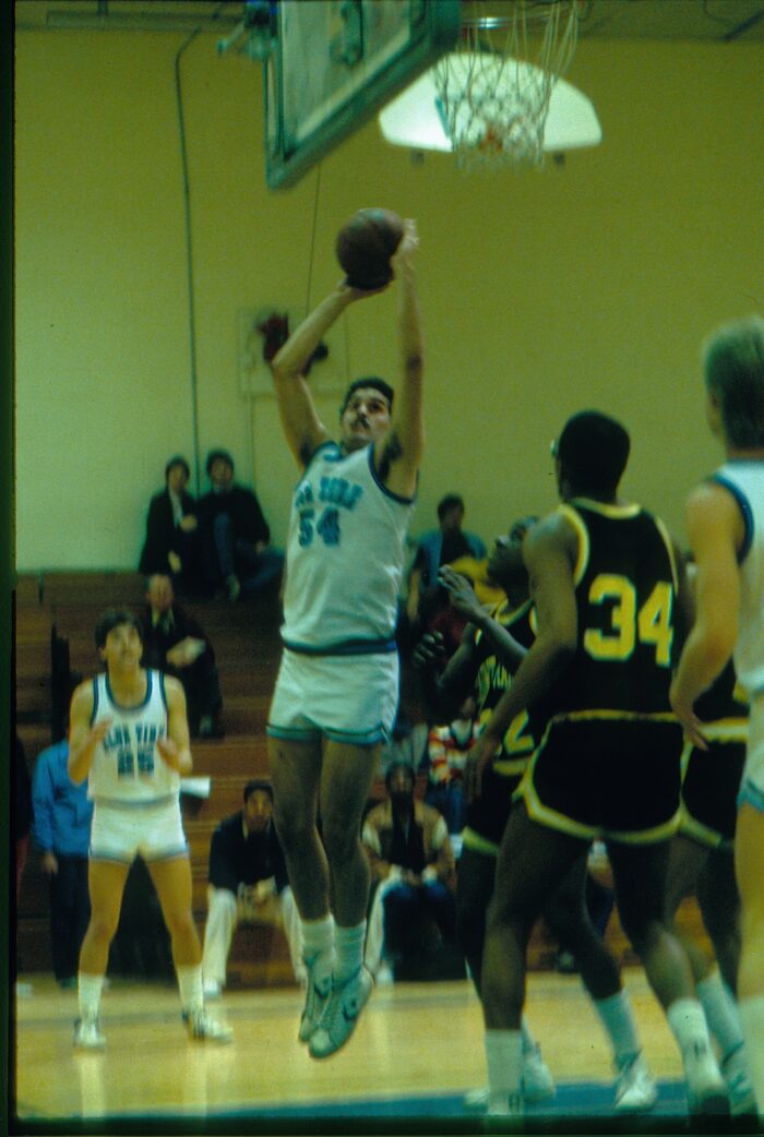 Player in a #54 Blue Tide jersey shown midair with arms extended going for a jump shot.