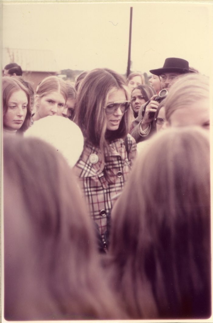 Gloria Steinem walking through a crowd of people. Several people are blocking the lower frame